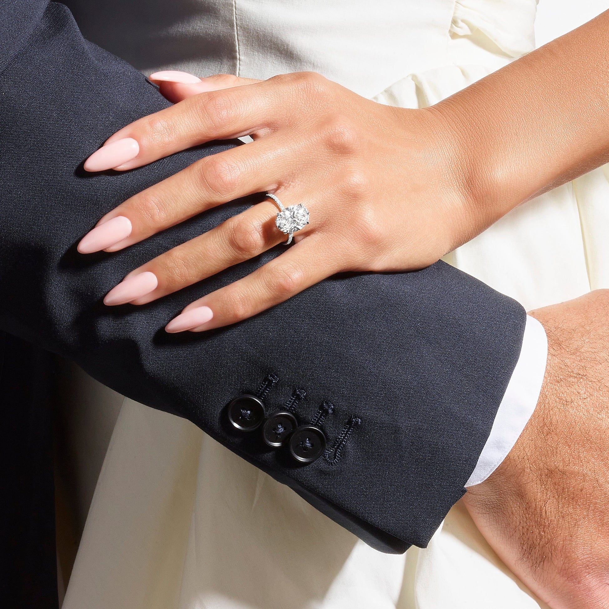 Hand with engagement ring on arm in a suit.