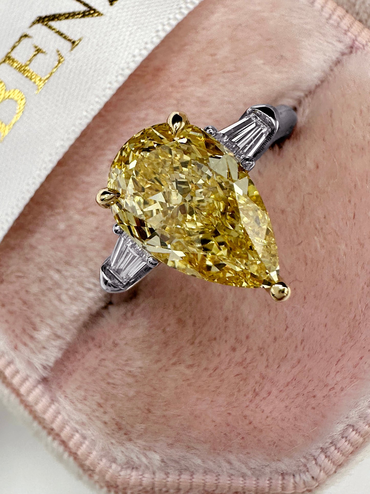 Yellow pear-shaped diamond ring on pink velvet.