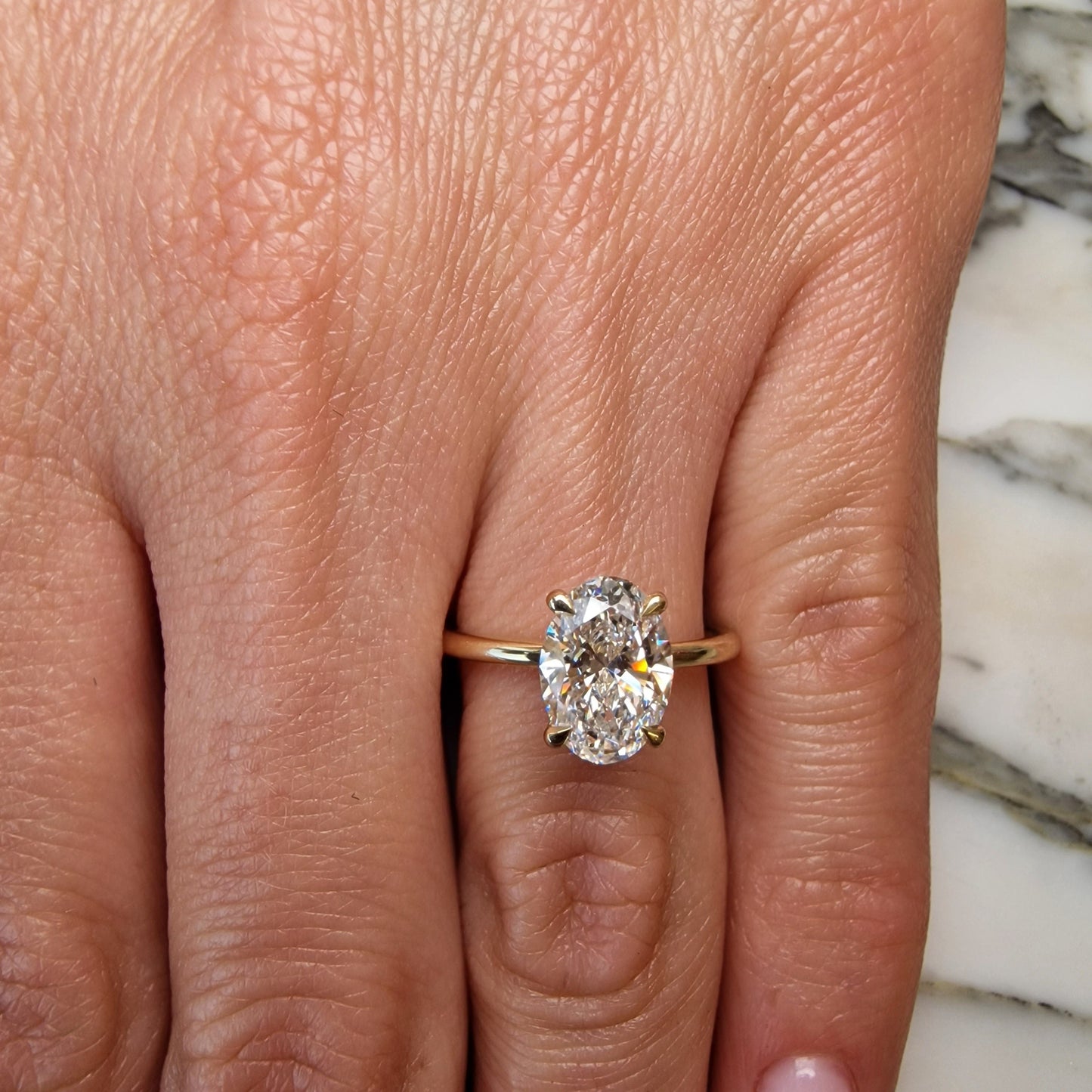 Hand wearing a gold ring with an oval diamond.