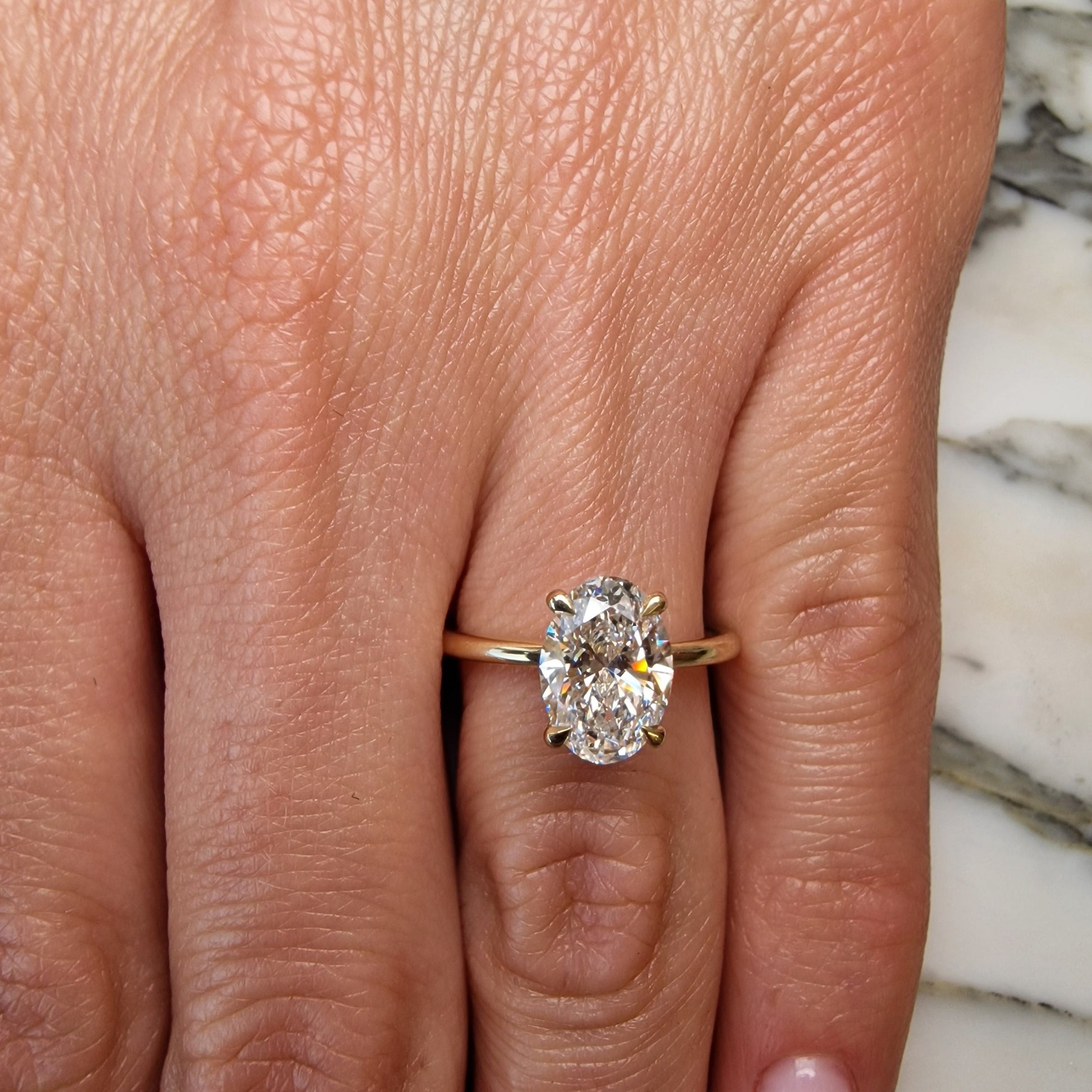 Hand wearing a gold ring with an oval diamond.