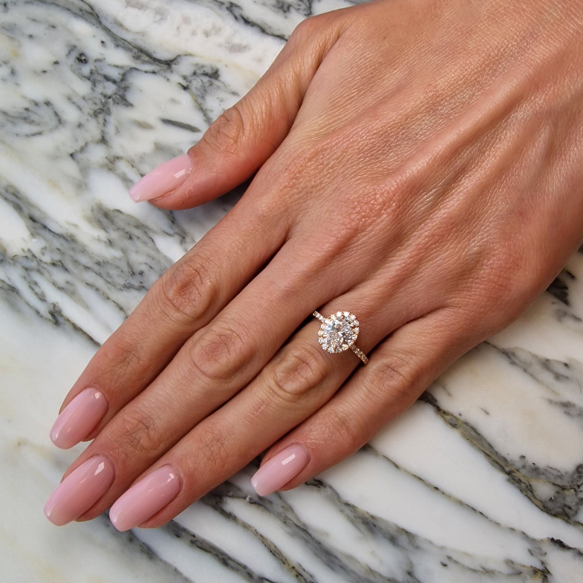 Hand with engagement ring on marble surface.