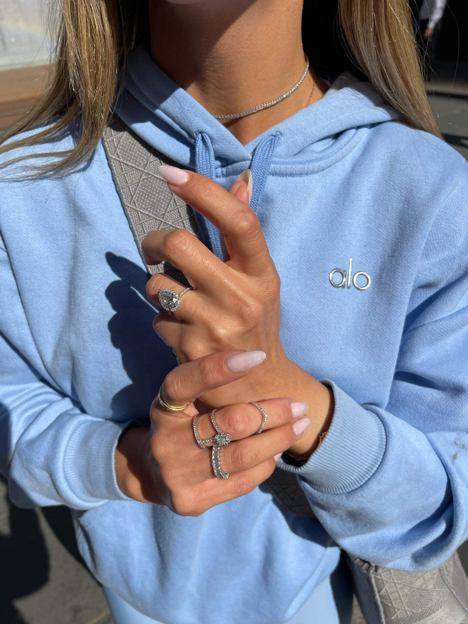 Woman wearing rings, a necklace, and a light blue hoodie.