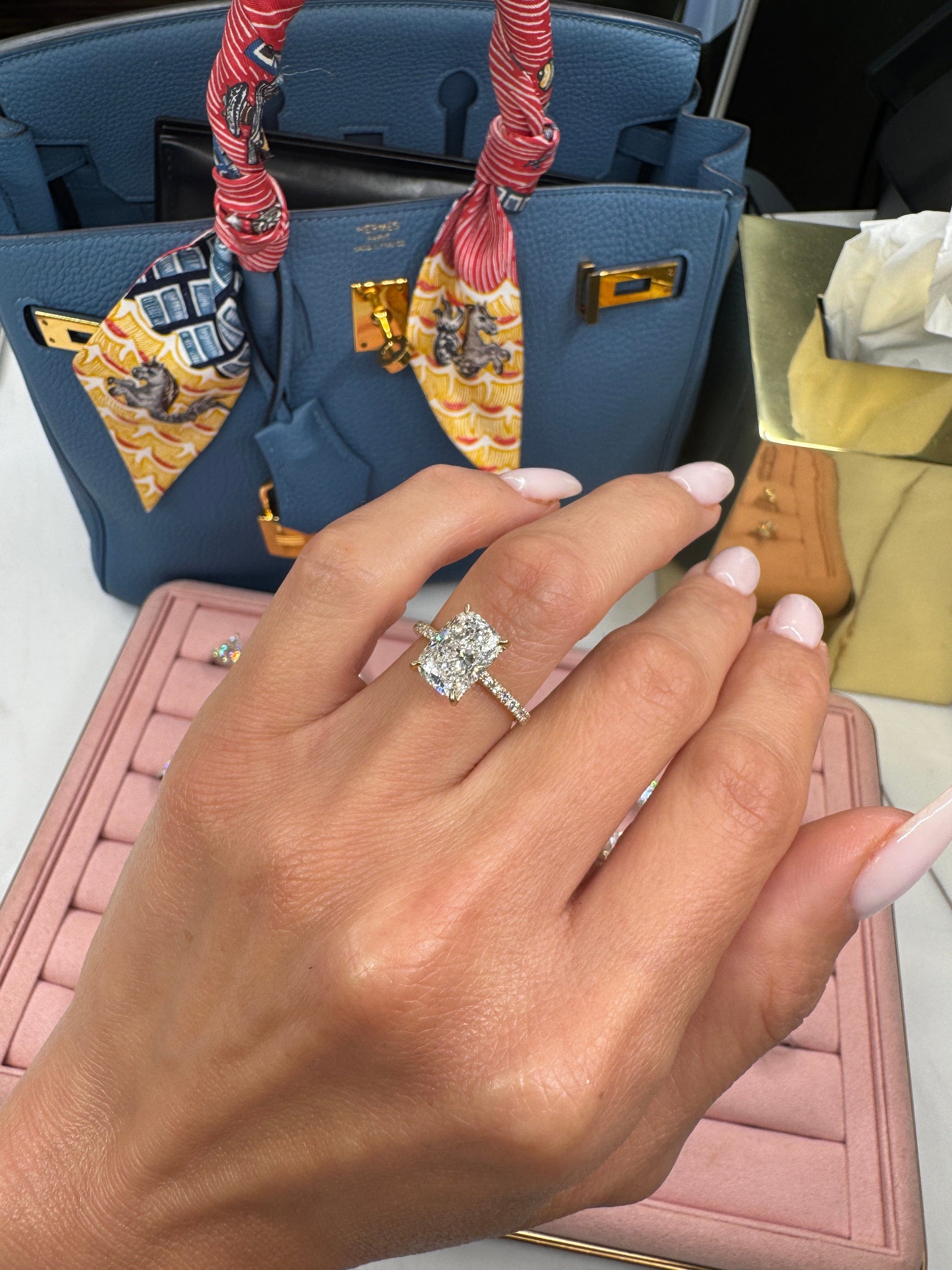 Hand with diamond ring next to a blue handbag.